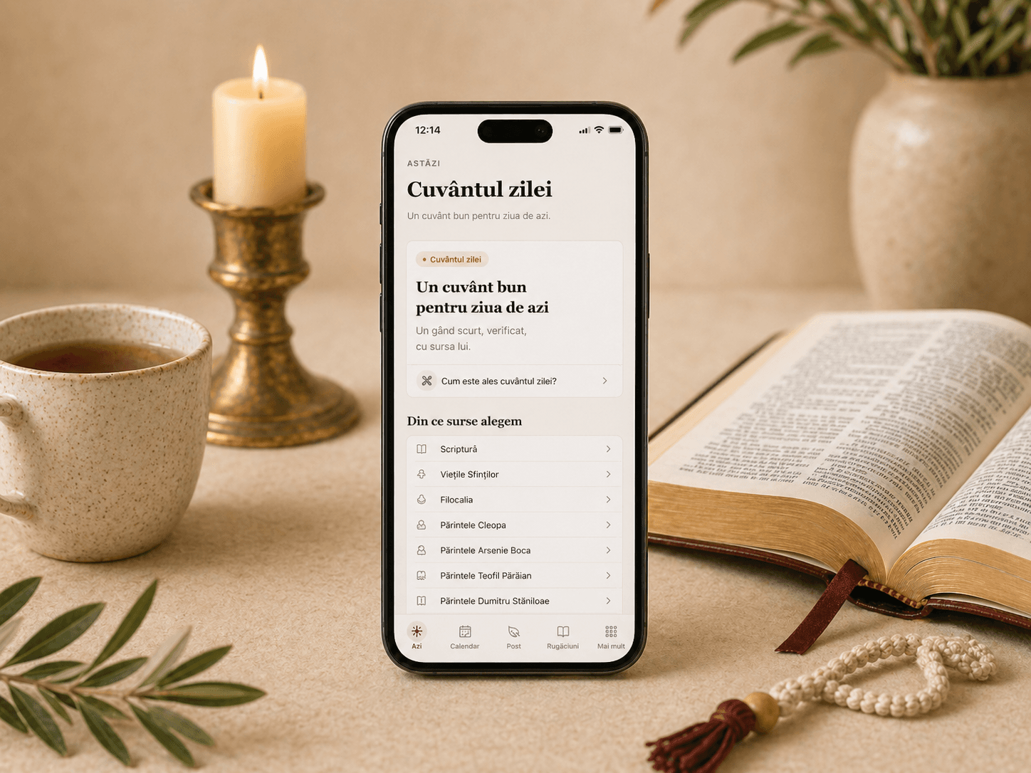 Telefon cu pagina „Cuvântul zilei” lângă o Biblie deschisă, lumânare, ceașcă de ceai și metanier.